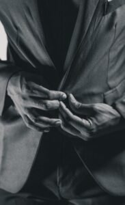Home A monochrome image showing a person buttoning a suit jacket, capturing the elegance and detail of formal wear.
